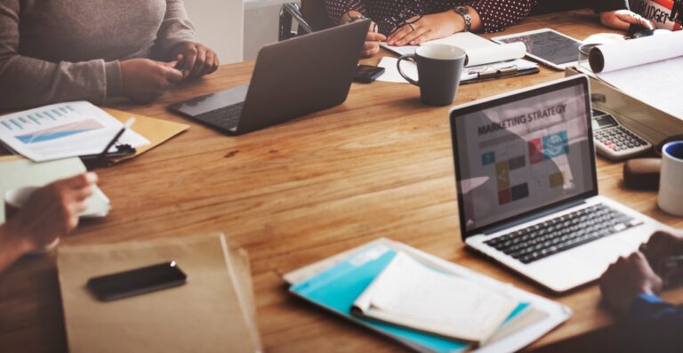 People review a clear infographic with charts, icons, and notes on a laptop and printed page.